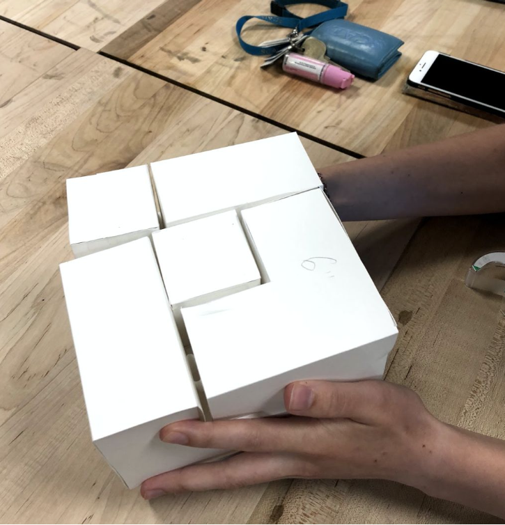 Hand testing the paper prototype: white cardboard cubes held and arranged on a wooden table, keys and a phone nearby.